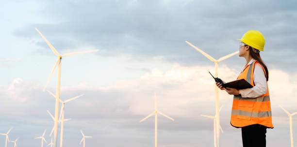 istock female engineer using walkie talkie and reading clipboard to checking system against wind turbine farm 1346486790