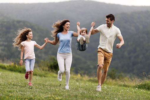 Carefree family having fun while holding hands and running in nature. Parents are swinging little boy. Copy space.