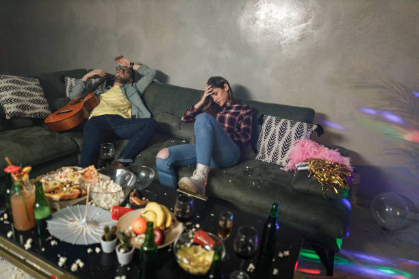 Drunk couple having a hangover after party at home. Young wasted couple having a headache after messy party at their home. after party stock pictures, royalty-free photos & images