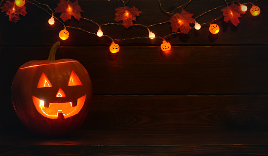 Glowing Halloween pumpkin with garlands on a wooden background. Halloween.Jack o lantern. Copy space. Trick or treat,