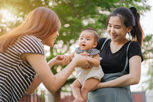 homosexual family of mothers hugs and plays with baby on a green bokeh background with sunlight
