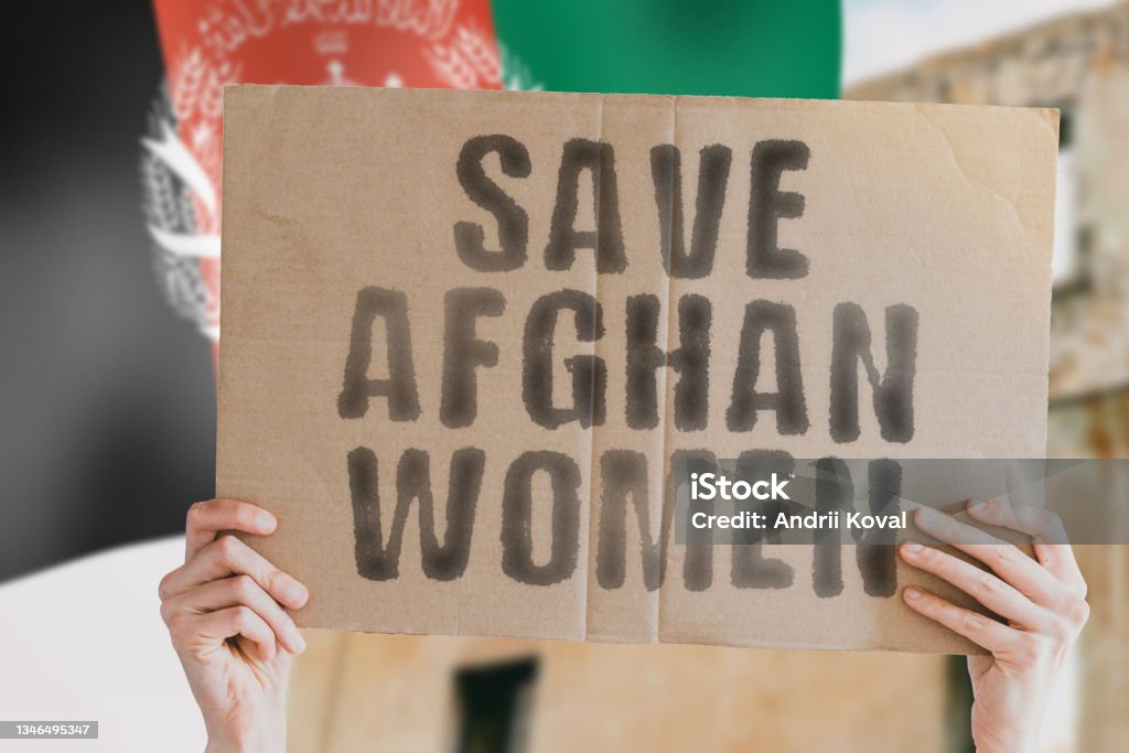 The phrase " Save afghan women " on a banner in men's hand with blurred Afghan flag on the background. Protest. Riot. Violence. Collapse. Politics. Streets. Save. Cruelty. Religion. Help. Afghanistan Women Stock Photo