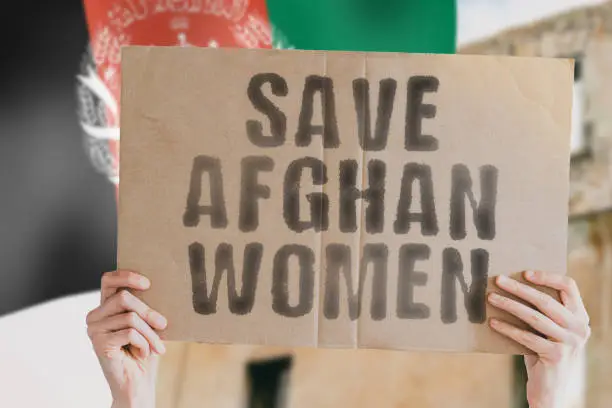 The phrase " Save afghan women " on a banner in men's hand with blurred Afghan flag on the background. Protest. Riot. Violence. Collapse. Politics. Streets. Save. Cruelty. Religion. Help. Afghanistan