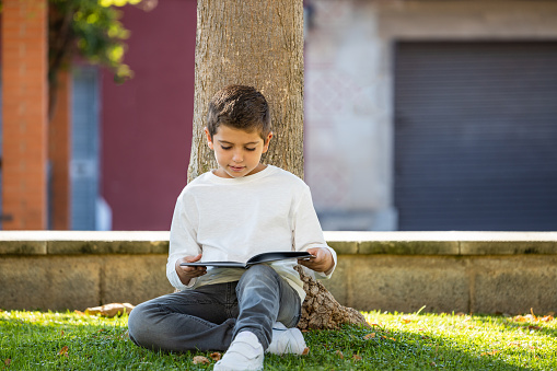 Little kid reading a book in a shade of a tree