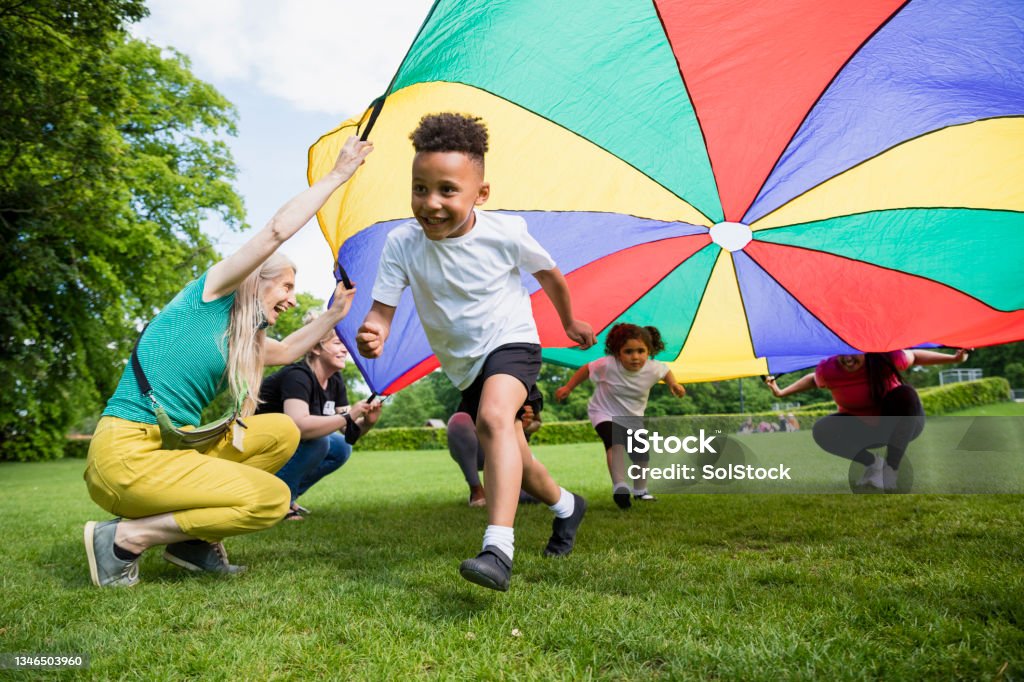 School Children with a Parachute Children playing with a parachute at school during pe in the North East of England. A boy is running underneath it. Playing Stock Photo