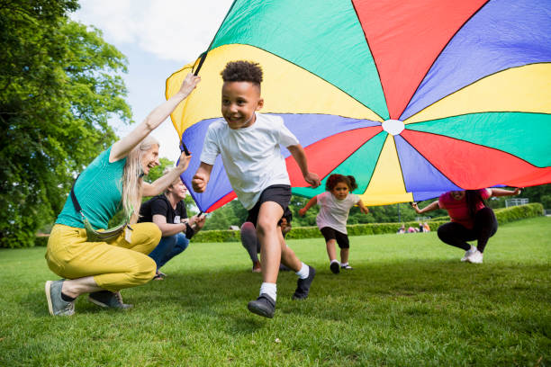 School Children with a Parachute Children playing with a parachute at school during pe in the North East of England. A boy is running underneath it. children stock pictures, royalty-free photos & images