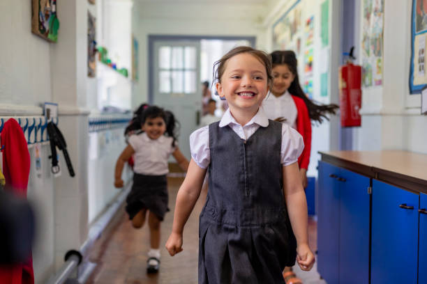 Having Fun at School Primary school students running down a hallway while at school in the North East of England. Focus is on a girl who is laughing, looking away from the camera with her friends out of focus behind her. primary school student stock pictures, royalty-free photos & images