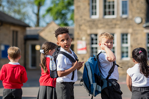 Rear view of children in their school yard going to their classes in the North East of England. Some are looking behind them, wearing their backpacks.