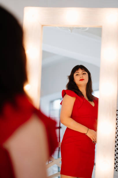 빨간 드레스를 입은 매력적인 통통한 여성이 거울을 본다. - mirror women dress looking 뉴스 사진 이미지