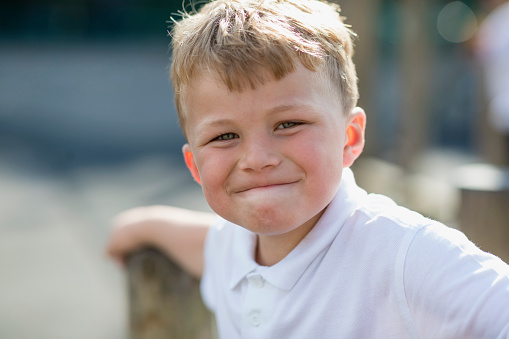 Close up of a boy looking at the camera smiling while playing in his school yard in the North East of England. The sun is shining.