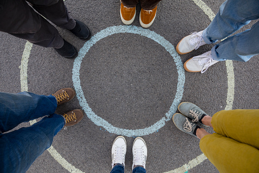 Directly above view of unrecognisable people standing in a circle, the view is on their feet. They are standing on a circle painted on the ground.