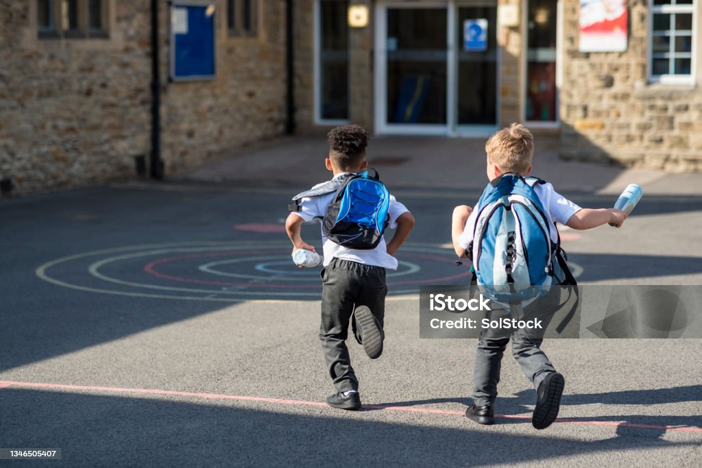 Running to School Rear view of two boys running in their school yard in the North East of England. They are running towards the door with their backpacks on. Elementary Student Stock Photo