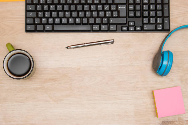 Computer keyboard, coffee cup, sticky note pen and headphones on the desk