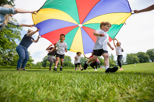 Children playing with a parachute at school during pe in the North East of England. The children are running underneath it.