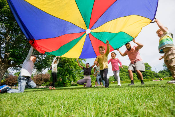 Preschool Parachute Time Children playing with a parachute at school during pe in the North East of England. A boy is running underneath it. two groups stock pictures, royalty-free photos & images