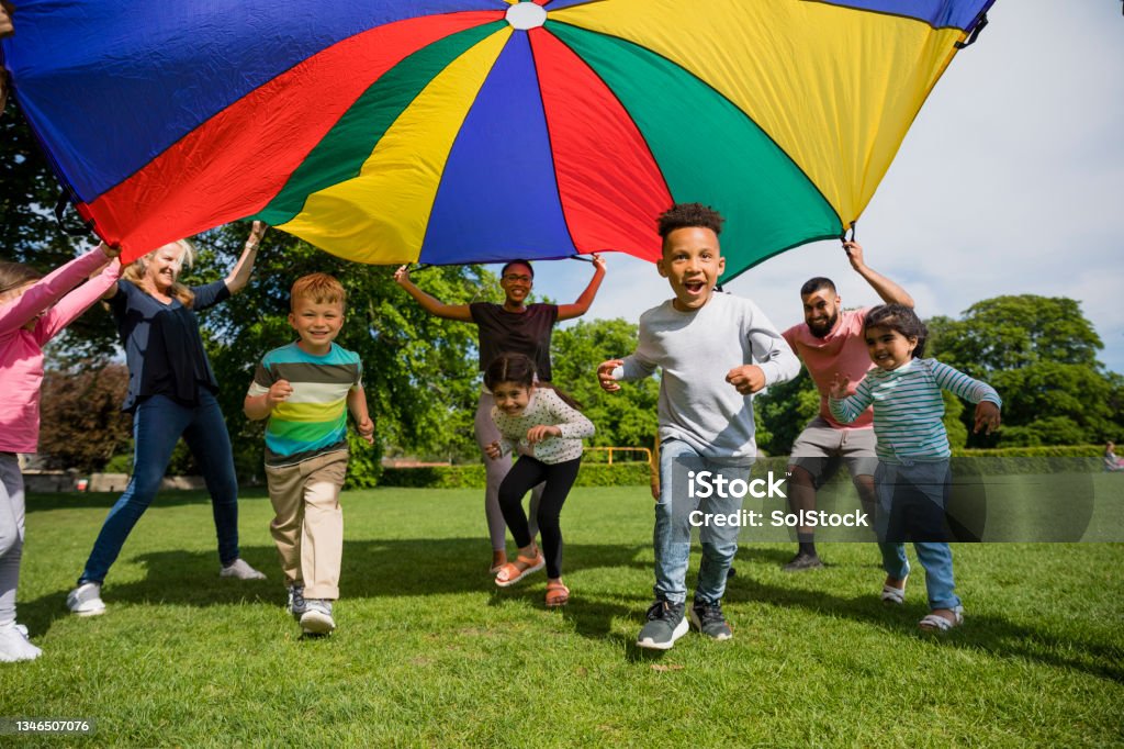 Quick! Run Under! Children playing with a parachute at preschool in the North East of England. The children are running underneath it. Excitement Stock Photo