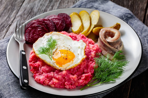 labskaus, corned beef, purée de pommes de terre avec la betterave garnie d’œufs au plat, betteraves tranchées, avec des cornichons et hareng roulé sur une assiette sur une table en bois, cuisine allemande, style hambourg - rollmops photos et images de collection