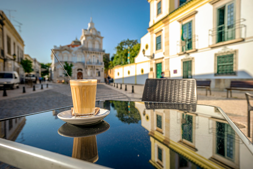 Coffee with milk called galao with landmark of Belmarco mansion in the background, Faro, Algarve, Portugal