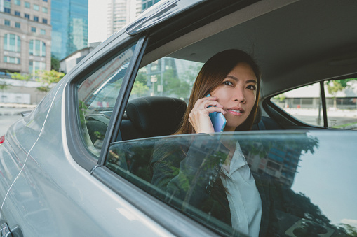 An Asian businesswoman making a call with smartphone in the back seat of car.
