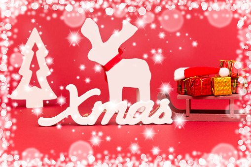 Xmas background in red and white, with a moose, presents on a sleigh, Christmas tree, Santa's hat and text x mas, framed with a bokeh of stars, snowflakes and spheres.