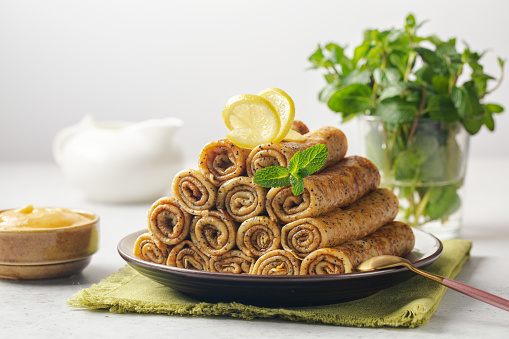 Pyramid of sweet crepe roll-ups with poppy seeds. Decorated with lemon and mint, lemon curd beside. White background.