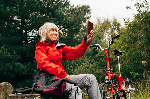 Mature woman on her mobile phone relaxing during a cycle cycling in the Culbin Forest in the Morayshire district of Scotland.