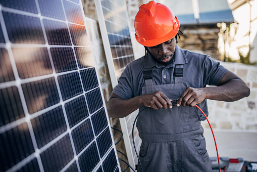 Male engineer with protective helmet preparing for installing solar panels. Professional electrician checking electricity of solar panels,