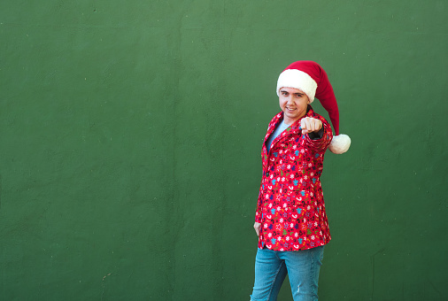 Man in christmas theme clothes pointing straight while smile standing in a green background