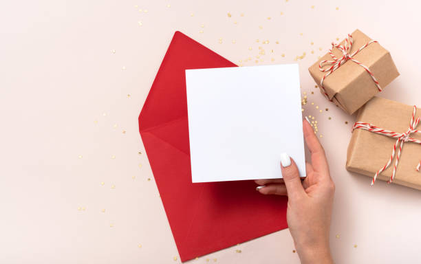 istock Female hand holds blank square paper mockup envelope red christmas 1346517633