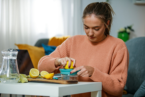 Copy space shot of young woman sitting on the living room floor and squeezing a lemon for a fresh lemonade that she is preparing.