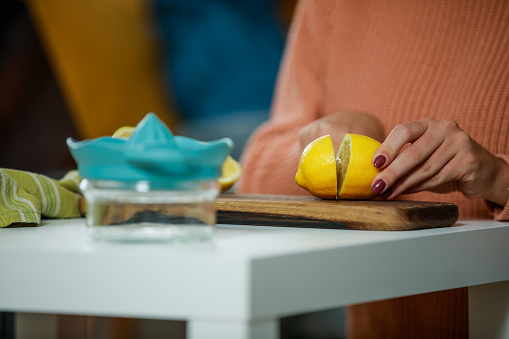 Copy space shot of unrecognizable woman sitting at the coffee table and cutting a lemon in half for a lemonade she is making.