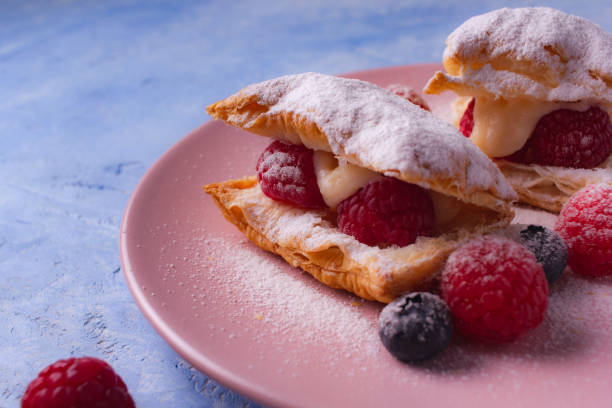 puff pastry with cream, raspberries, blueberries and sugar powder on light blue background. - powder puff imagens e fotografias de stock