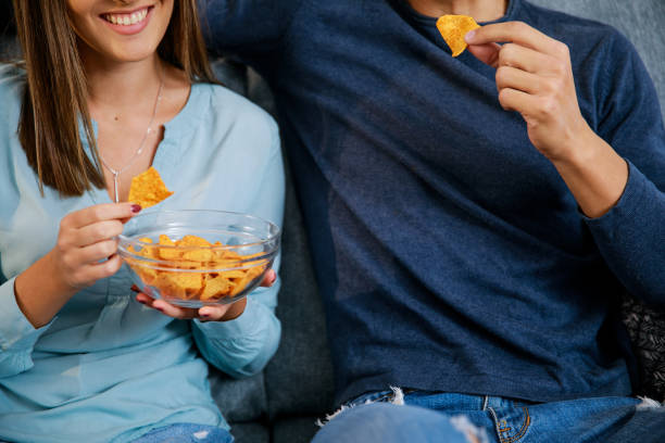istock Cut out shot of couple snacking on tortilla chips while watching TV 1346521215