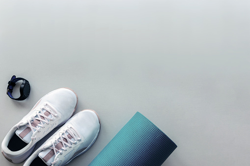 White sneakers, sport watch and yoga mat on light gray background. Concept of healthy life, sport and training. Top view, flat lay. Copy space.