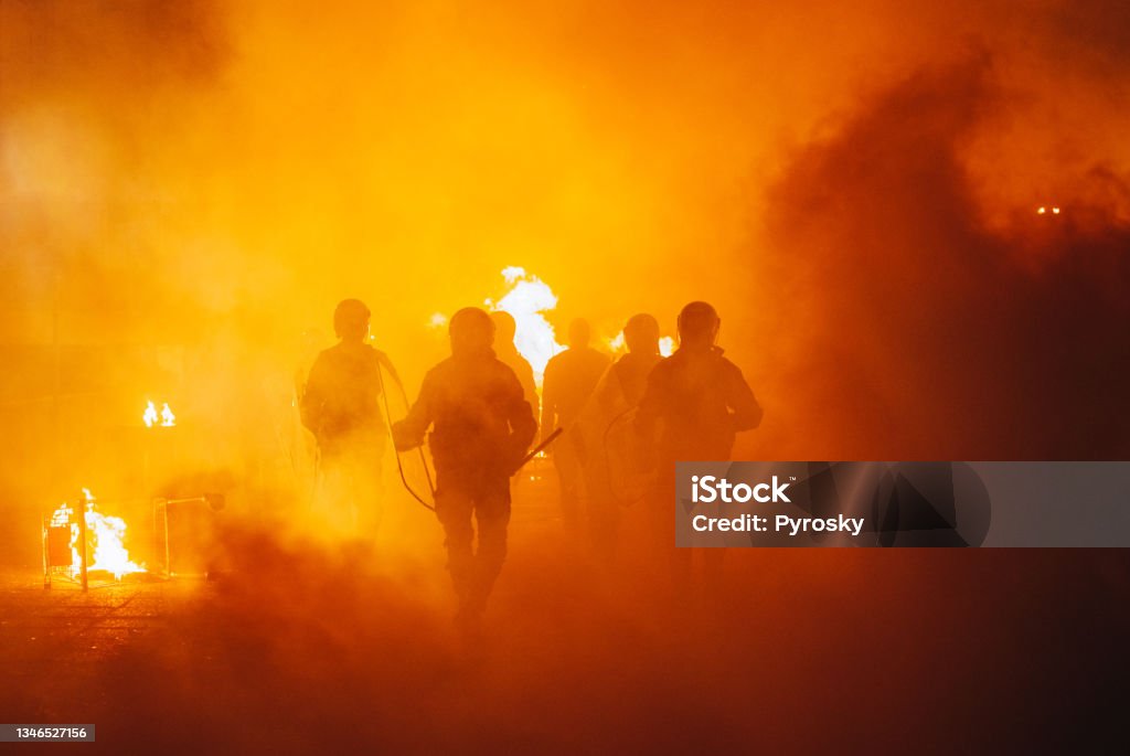 Riot In The City Silhouette of armored police officers  running  in front of the fire War Stock Photo