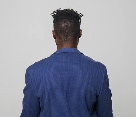 Rear view of young businessman wearing blazer while standing against gray background.