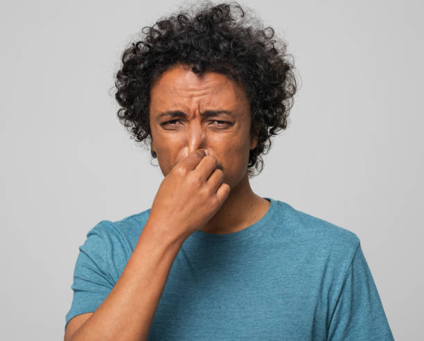 Close-up of young man holding nose Portrait of young man holding nose while standing against gray background. holding nose stock pictures, royalty-free photos & images