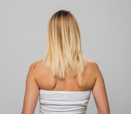 Rear view of mature woman standing against gray background.
