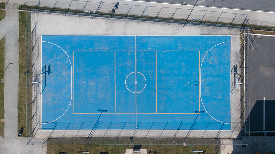 Sports court with various modalities (futsal, basketball, volleyball...) seen from above, in a photo taken with a drone, in blue color with flaws in the paint due to use.