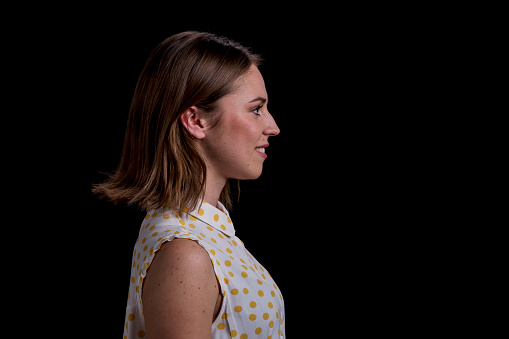 Side view of young woman standing against black background.