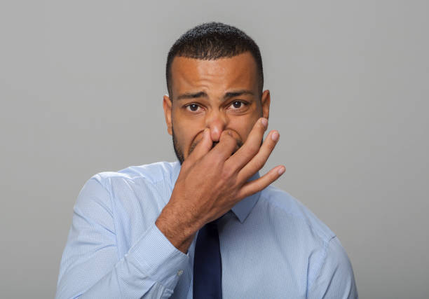 Close-up of mid adult businessman holding his nose Portrait of mid adult businessman holding his nose while standing against gray background. holding nose stock pictures, royalty-free photos & images
