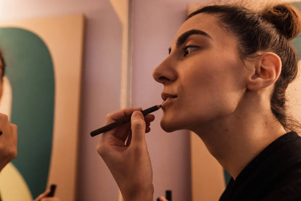 istock Woman observing herself in the mirror while applying a lip liner 1346533656