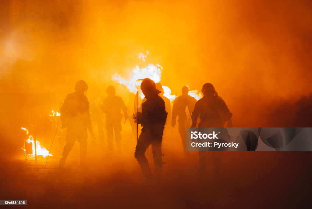 Riot On The City Streets Silhouette of armored police officers  running  in front of the fire Protest Stock Photo