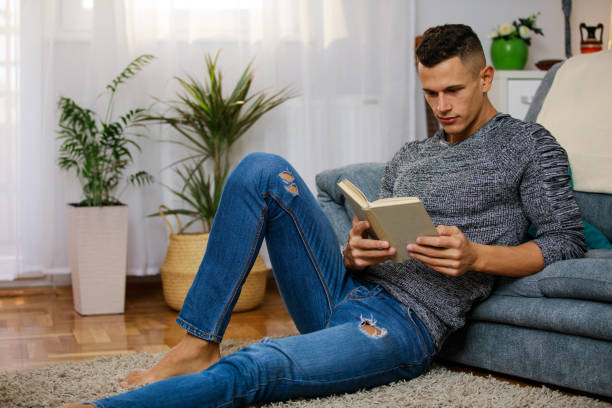 istock Young man sitting on the floor and reading a book 1346537921