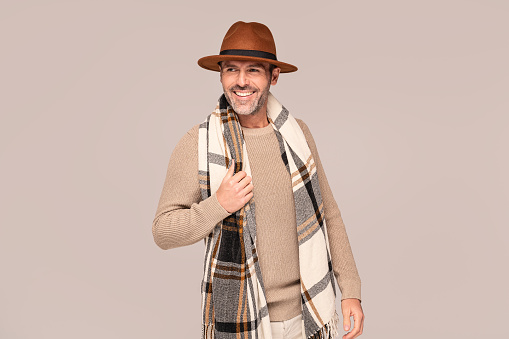 Cheerful handsome guy in fashionable autumn clothes, hat and scarf, posing in studio. Happy bearded man with beautiful smile. A lot of copy space.