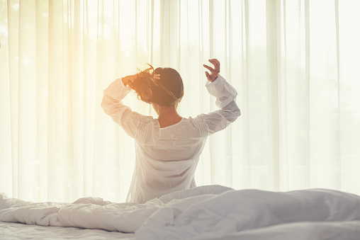 Asian women waking up stretching and raise arms in bed room at home. Young people early morning time and sunny day. Lifestyle Concept