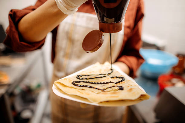 Making Pancakes Woman pouring a chocolate topping over a pancake crepe stock pictures, royalty-free photos & images