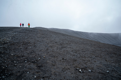 Tourists hiking on the top of crater Hverfjall with cloudy sky in background. North Iceland. Hverfjall,  is one of the best preserved circular volcanic craters in the world and it is possible to walk around and inside it.