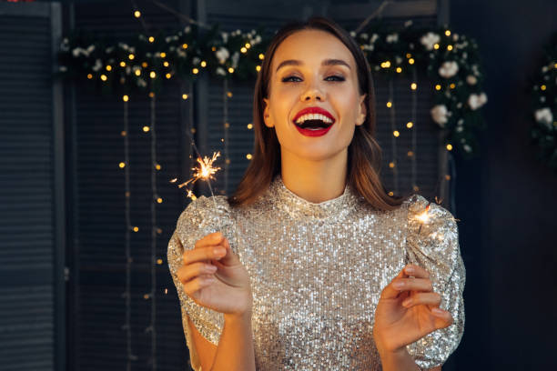 happy beautiful woman holding festive sparkler among christmas night - christmas december holiday holidays and celebrations imagens e fotografias de stock