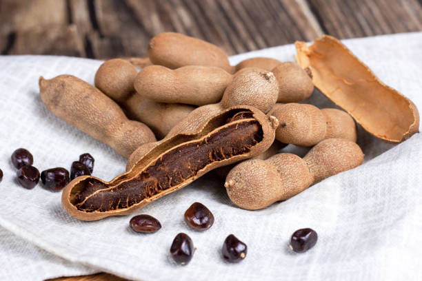 istock Fresh brown tamarind fruit pods ripe with seeds on light textile background close up 1346544434